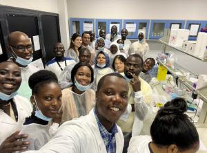 A selfie of the attendees in a lab, they are all smiling and wearing white lab coats